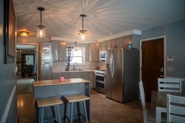 kitchen featuring sink, appliances with stainless steel finishes, backsplash, hanging light fixtures, and a kitchen island