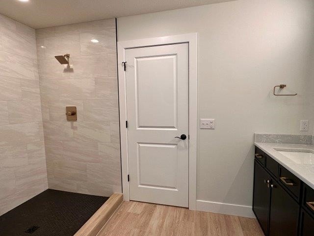 bathroom featuring a tile shower, vanity, and wood-type flooring