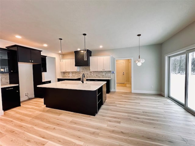 kitchen with decorative backsplash, light wood-type flooring, sink, white cabinets, and an island with sink