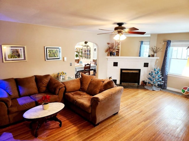 living room featuring light wood-type flooring, a brick fireplace, and ceiling fan