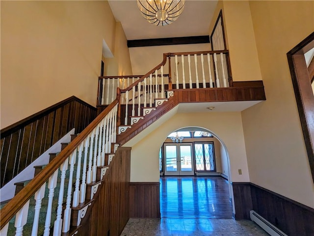 stairs featuring a notable chandelier, french doors, a towering ceiling, and a baseboard heating unit