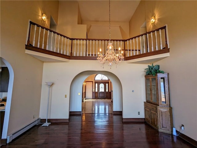 unfurnished living room featuring dark hardwood / wood-style flooring, a baseboard radiator, a high ceiling, and a notable chandelier