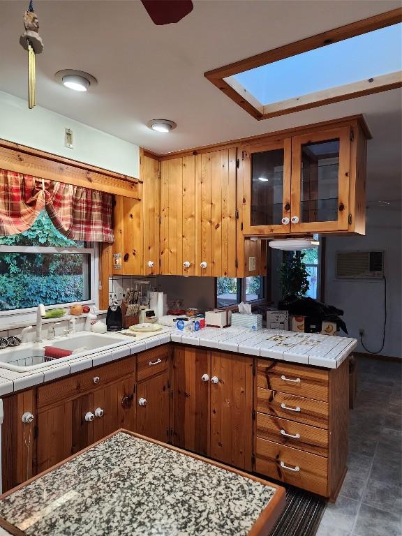 kitchen with tile countertops, a skylight, kitchen peninsula, and sink