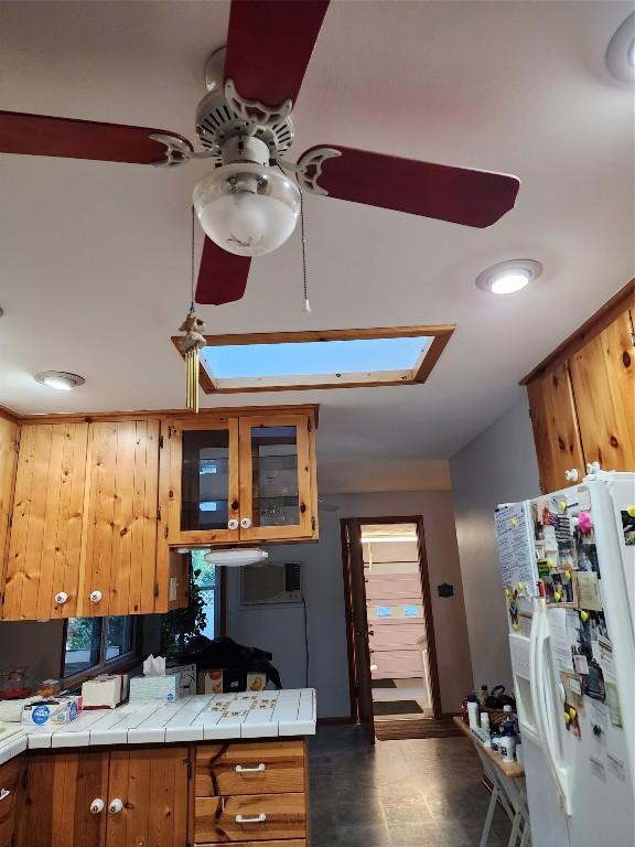 kitchen featuring ceiling fan, tile countertops, white refrigerator with ice dispenser, and a skylight