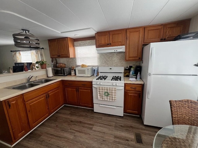 kitchen featuring visible vents, under cabinet range hood, brown cabinetry, white appliances, and a sink