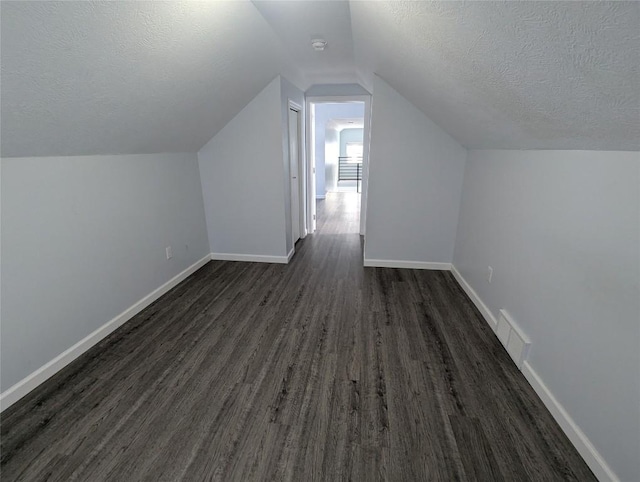 additional living space featuring lofted ceiling, dark hardwood / wood-style flooring, and a textured ceiling