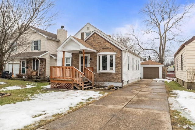 view of front facade with stone siding, an outdoor structure, driveway, and a detached garage