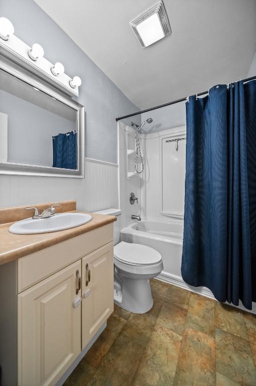 bathroom featuring visible vents, toilet, a wainscoted wall, shower / bath combination with curtain, and vanity