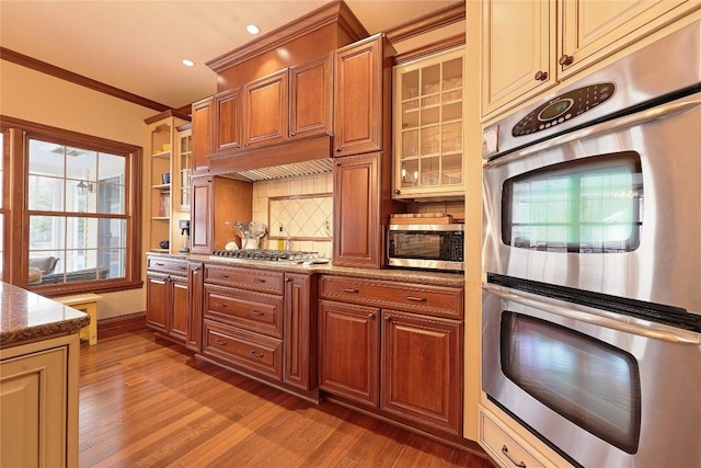 kitchen featuring light wood-type flooring, light stone countertops, ornamental molding, and appliances with stainless steel finishes