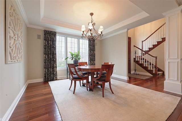 dining space with dark wood-type flooring, a tray ceiling, an inviting chandelier, and ornamental molding