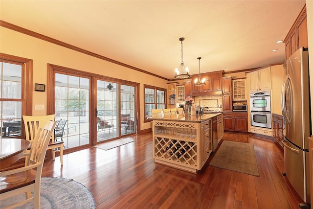 kitchen featuring hanging light fixtures, tasteful backsplash, a center island with sink, appliances with stainless steel finishes, and ornamental molding