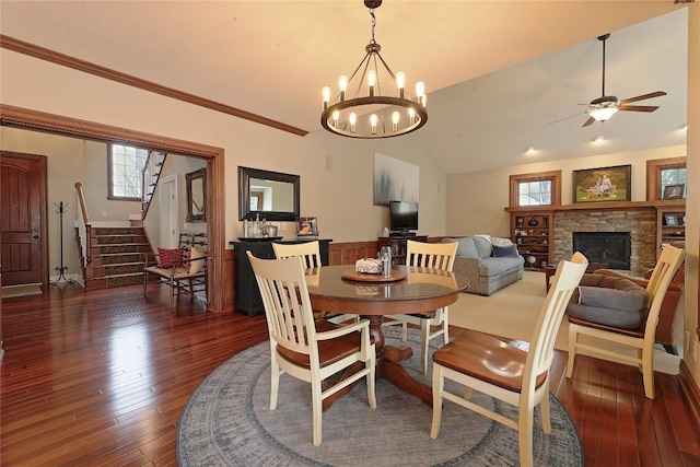 dining area featuring a fireplace, ceiling fan with notable chandelier, dark wood-type flooring, and lofted ceiling