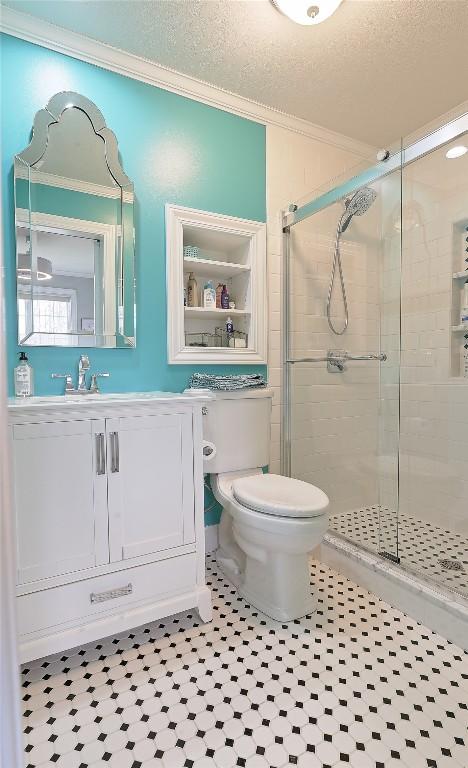 bathroom with ornamental molding, vanity, a textured ceiling, toilet, and a shower with shower door