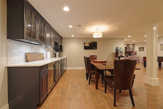 kitchen with decorative columns, light hardwood / wood-style floors, decorative backsplash, a fireplace, and dark brown cabinets