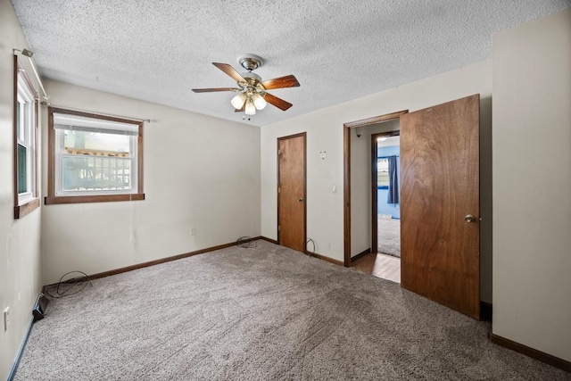 unfurnished bedroom featuring ceiling fan, light colored carpet, multiple windows, and a textured ceiling