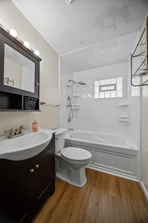 full bathroom featuring shower / washtub combination, hardwood / wood-style floors, vanity, toilet, and a textured ceiling