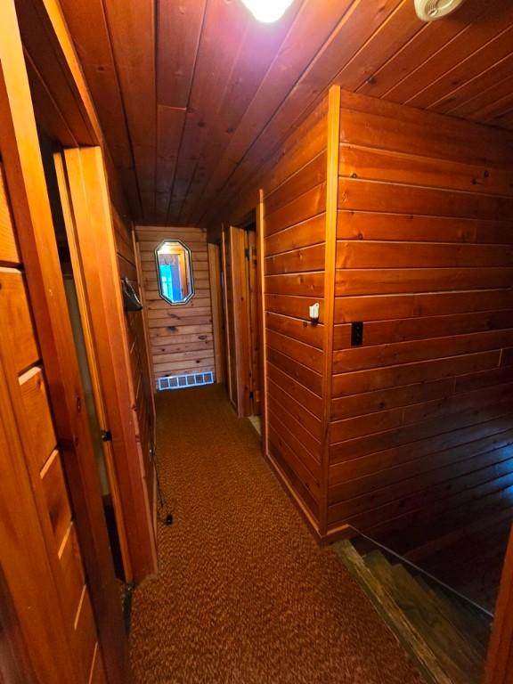 hall with dark colored carpet, wooden walls, and wood ceiling