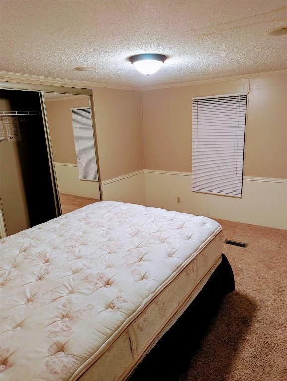 carpeted bedroom with a closet, ornamental molding, and a textured ceiling