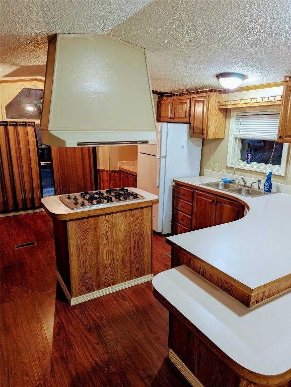 kitchen with a kitchen island, dark hardwood / wood-style floors, sink, gas stovetop, and a textured ceiling