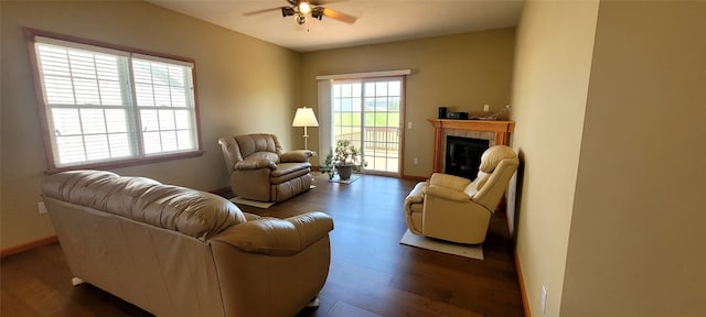 living area featuring a ceiling fan, baseboards, dark wood finished floors, and a tiled fireplace