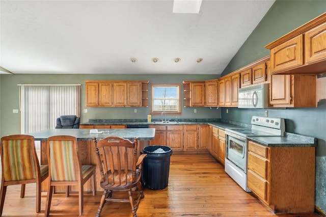 kitchen featuring light wood-type flooring, vaulted ceiling with skylight, a breakfast bar, white appliances, and sink