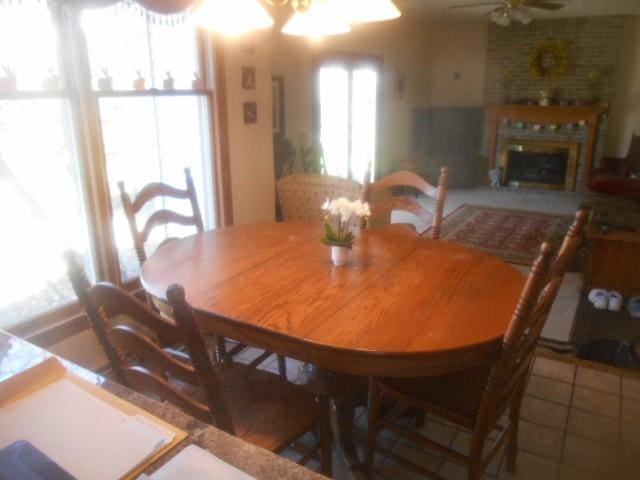 tiled dining space featuring a ceiling fan and a brick fireplace