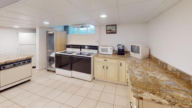 kitchen with a paneled ceiling, light stone counters, white appliances, light tile patterned floors, and cream cabinetry