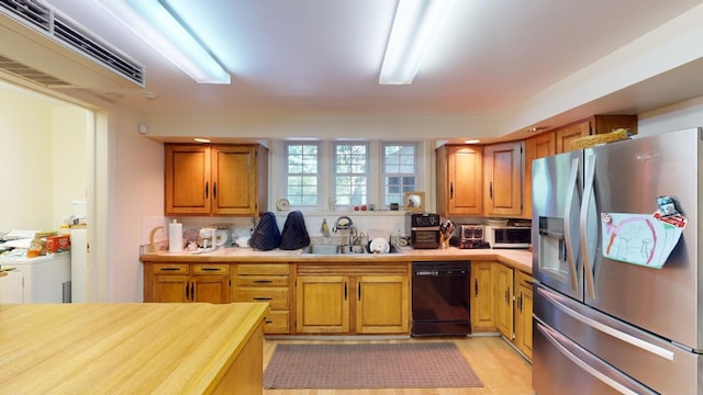 kitchen featuring dishwasher, sink, stainless steel fridge with ice dispenser, washer / clothes dryer, and light hardwood / wood-style floors