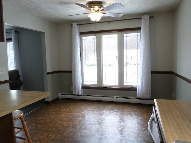 unfurnished dining area with baseboard heating, dark parquet flooring, and ceiling fan