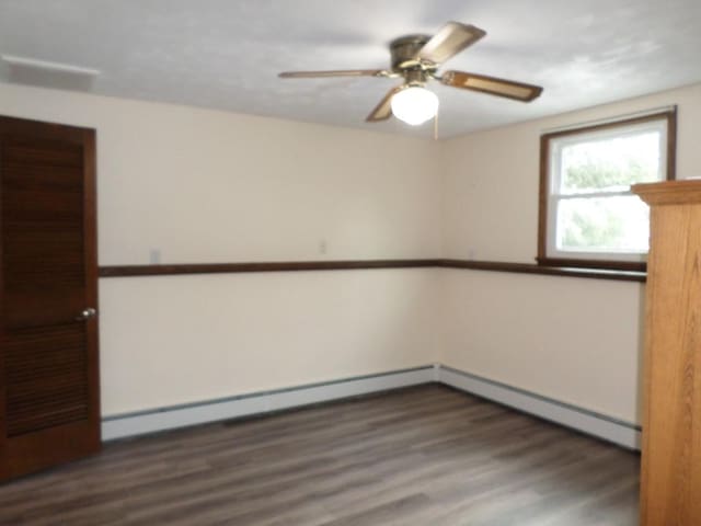 spare room with ceiling fan, dark hardwood / wood-style floors, and a baseboard heating unit