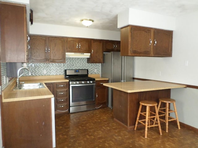 kitchen with dark parquet floors, sink, decorative backsplash, appliances with stainless steel finishes, and a kitchen bar