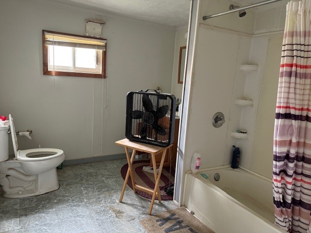 bathroom with shower / bath combo, a textured ceiling, and toilet