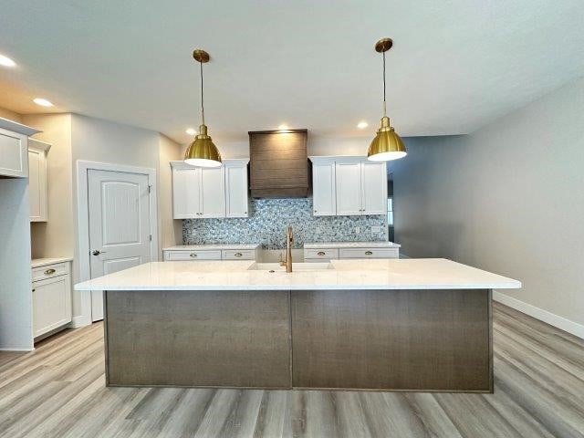 kitchen with custom range hood, white cabinetry, sink, and decorative light fixtures