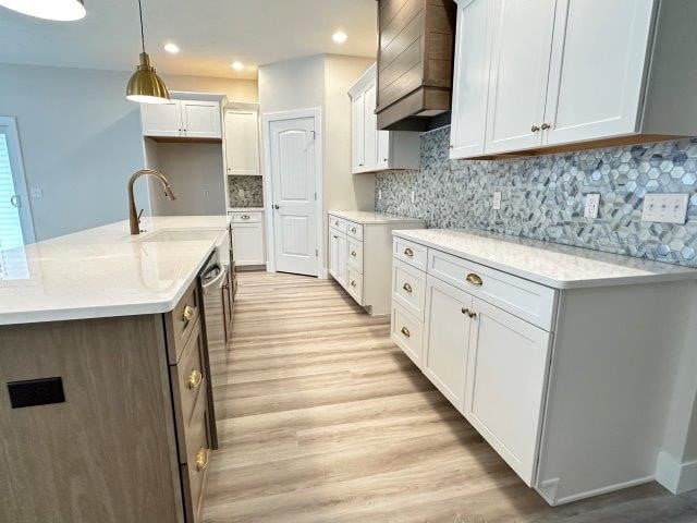 kitchen with premium range hood, sink, light hardwood / wood-style flooring, decorative light fixtures, and white cabinetry