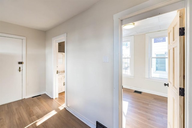 hallway with baseboards, visible vents, and wood finished floors