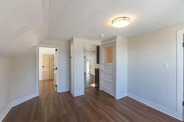 unfurnished bedroom with dark wood-style flooring, vaulted ceiling, and baseboards