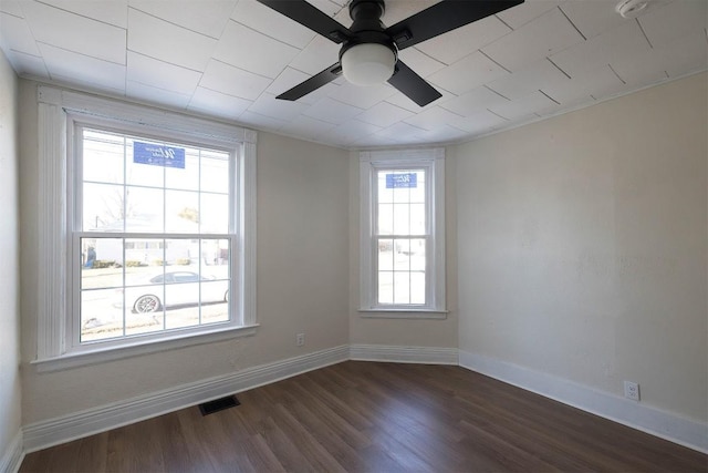 unfurnished room with a ceiling fan, visible vents, dark wood finished floors, and baseboards