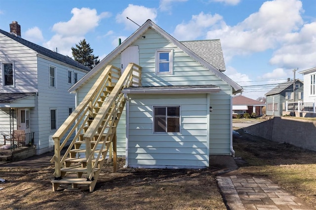 back of property with roof with shingles and stairs