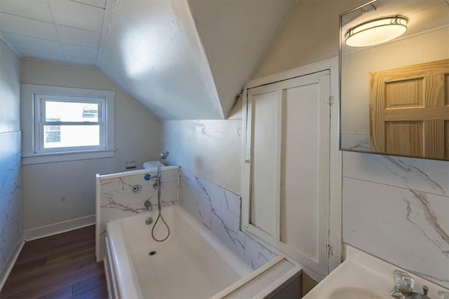 full bath featuring lofted ceiling, wood finished floors, a bathing tub, and baseboards