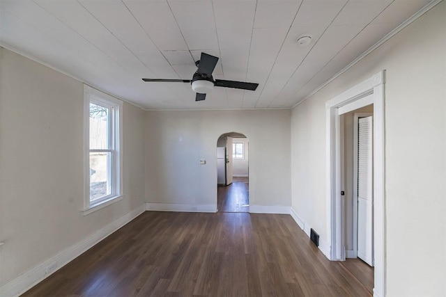 empty room featuring baseboards, visible vents, arched walkways, a ceiling fan, and dark wood-style flooring