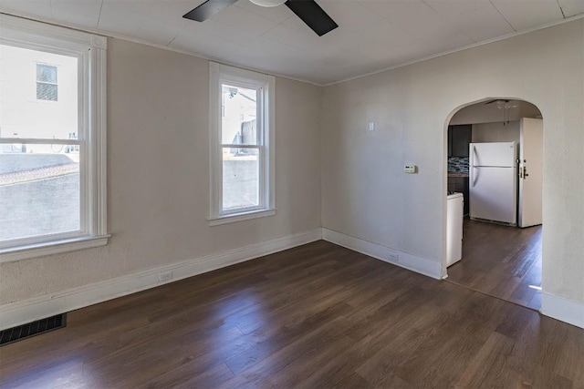 spare room featuring arched walkways, a wealth of natural light, dark wood-style flooring, and visible vents