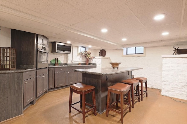 bar with a paneled ceiling, dark brown cabinetry, dark stone countertops, and appliances with stainless steel finishes