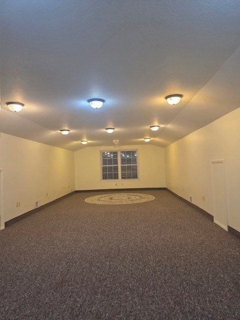 spare room with vaulted ceiling, dark carpet, and a textured ceiling