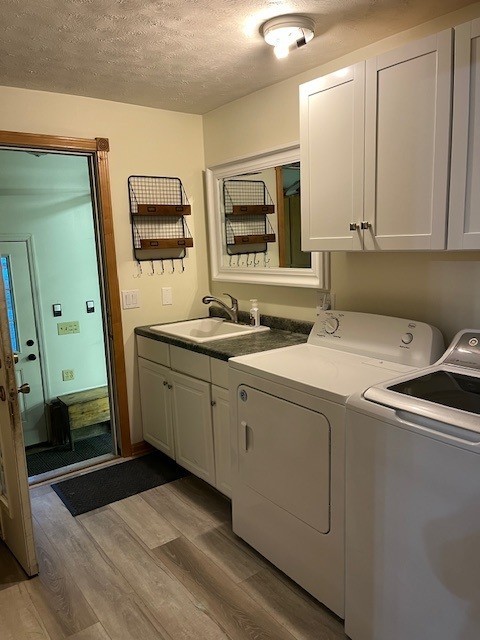 laundry area with wood finished floors, cabinet space, a sink, a textured ceiling, and washer and clothes dryer