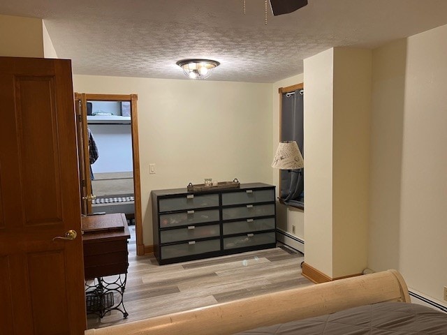 bedroom with light wood-style floors, a textured ceiling, and a baseboard radiator