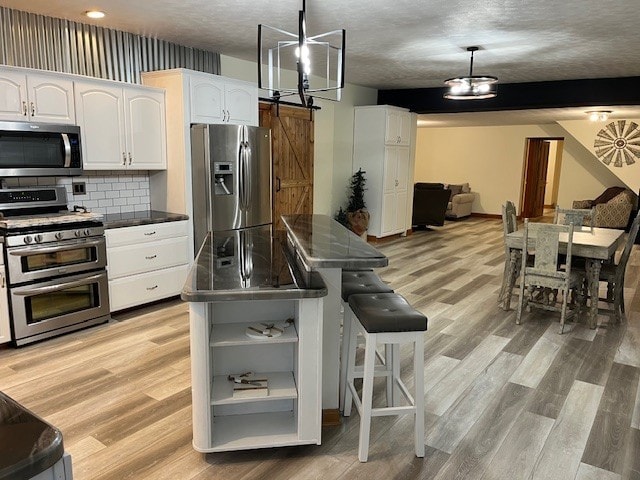 kitchen with dark countertops, white cabinets, stainless steel appliances, and light wood-style floors