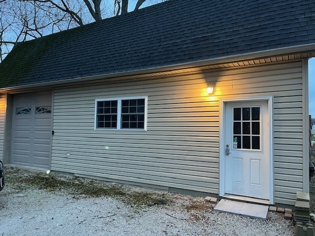 entrance to property featuring a garage and roof with shingles