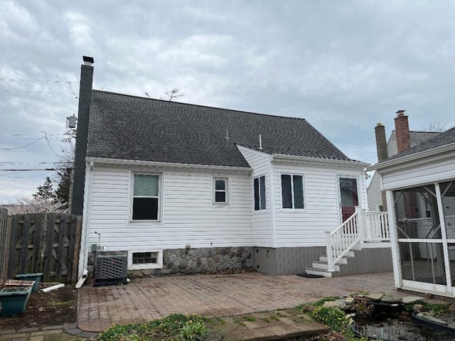 back of house with central air condition unit, a chimney, fence, a patio area, and a shingled roof