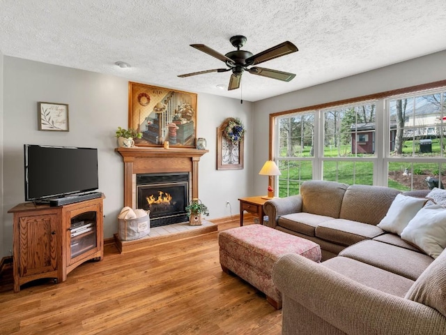 living area featuring a textured ceiling, a glass covered fireplace, ceiling fan, and light wood finished floors