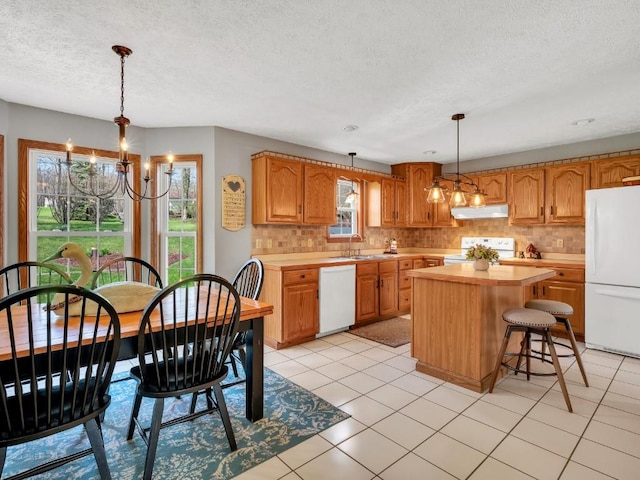 kitchen featuring white appliances, light countertops, under cabinet range hood, a sink, and a notable chandelier